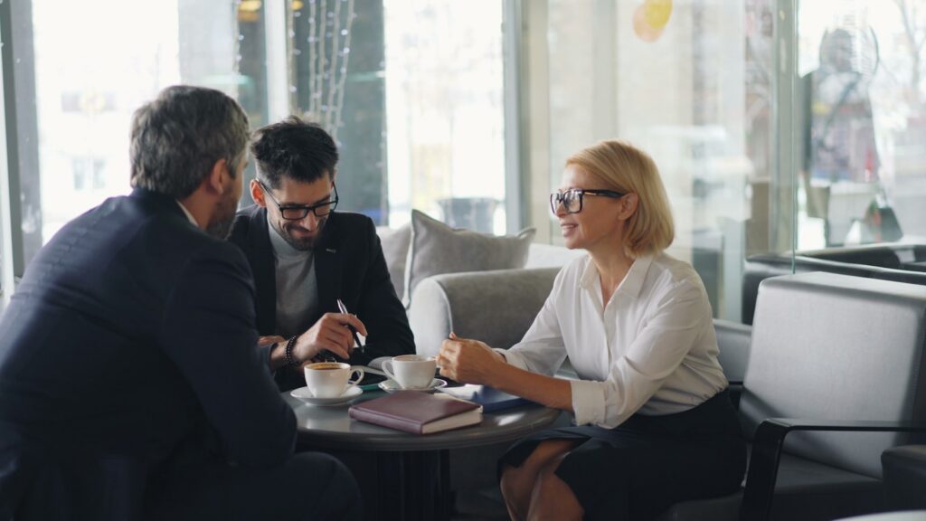 two men and a woman sitting at a table having a conversation
