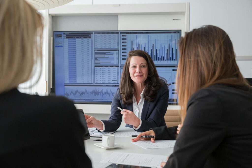 Professional businesswomen engaged in a meeting discussing data on a screen.