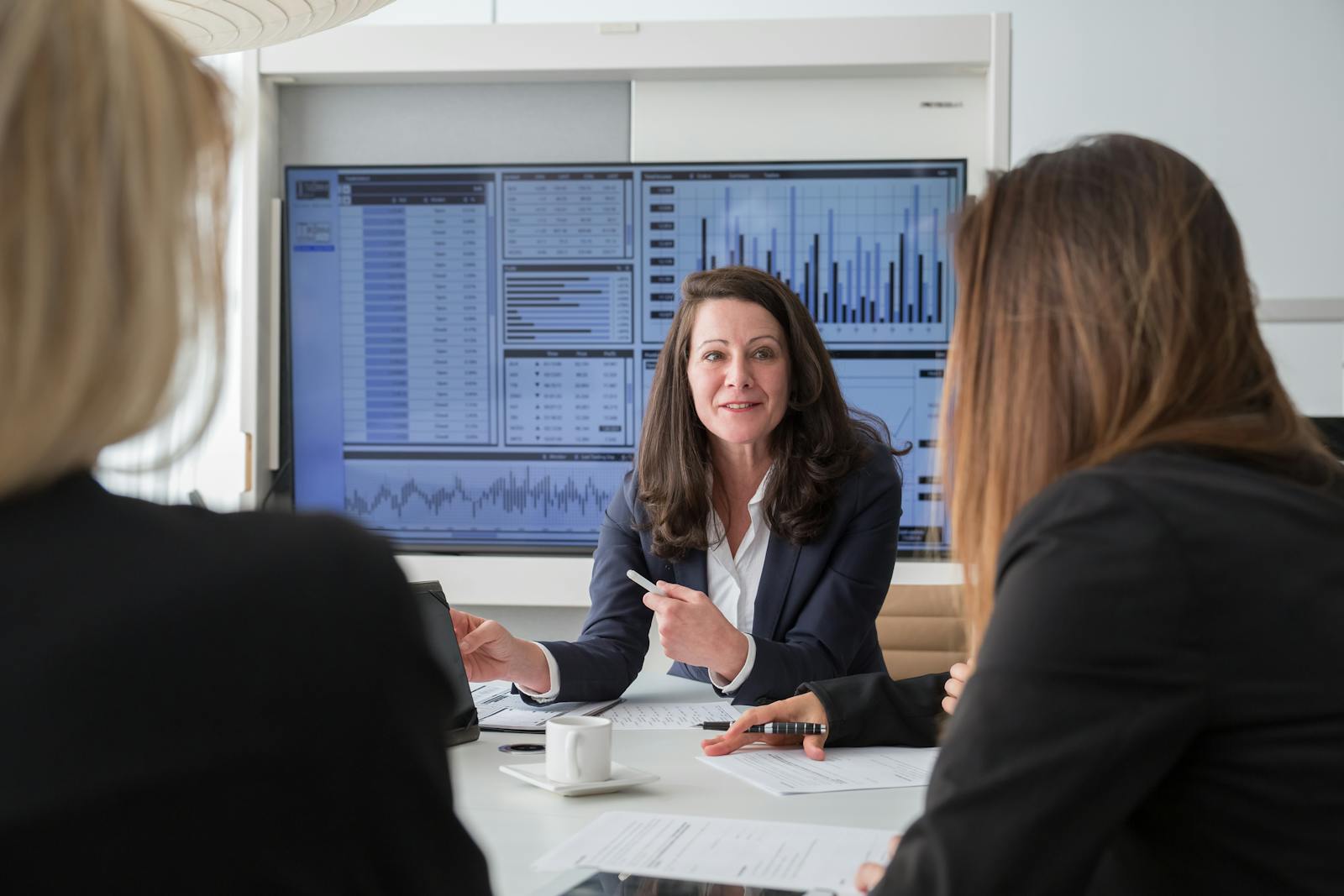 Professional businesswomen engaged in a meeting discussing data on a screen.