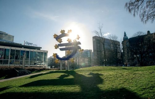 Euro sculpture in Frankfurt, Germany with cityscape buildings and sunlight.