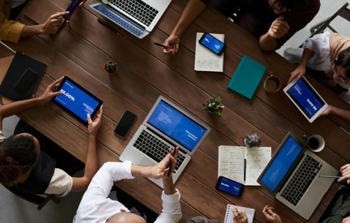 Overhead view of a diverse team discussing around a wooden table, using technology.