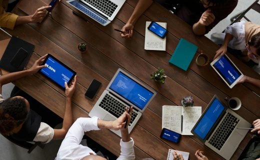 Overhead view of a diverse team discussing around a wooden table, using technology.