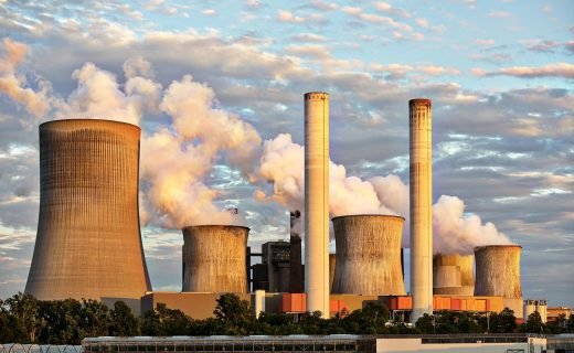 View of a power plant with smoke emissions under a cloudy sky, depicting industrial energy production.