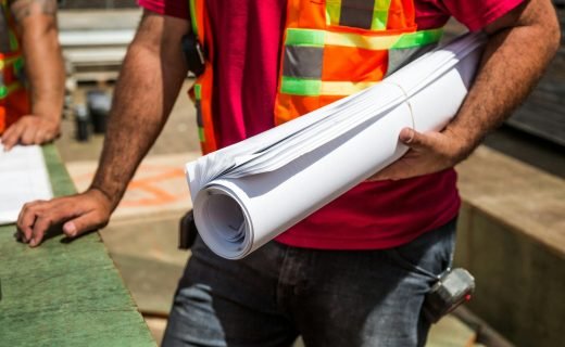 Construction workers in safety vests holding blueprints at a site during the day.