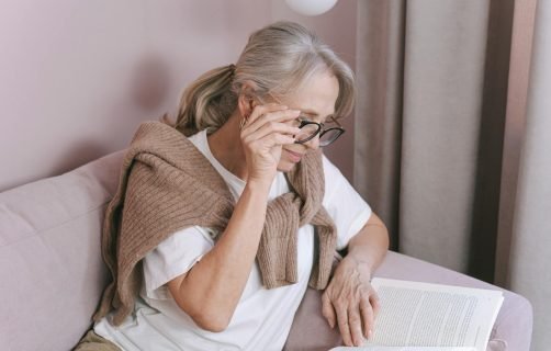 Elderly woman with glasses reading on a couch for leisure at home.