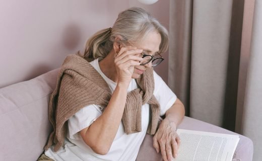 Elderly woman with glasses reading on a couch for leisure at home.