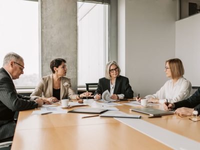 Five business professionals engaged in a meeting in a modern office setting, discussing documents and ideas.