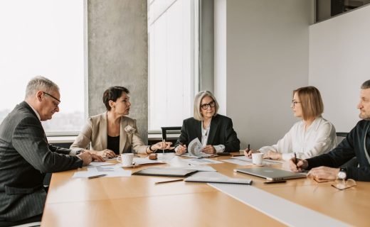 Five business professionals engaged in a meeting in a modern office setting, discussing documents and ideas.