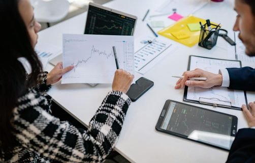 Two colleagues analyzing financial graphs during a business meeting in a modern office setting.