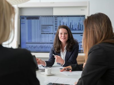 Professional businesswomen engaged in a meeting discussing data on a screen.