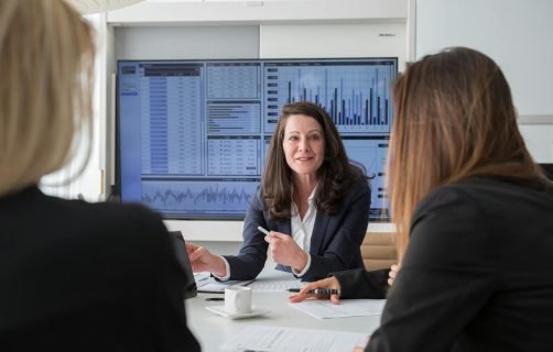 Professional businesswomen engaged in a meeting discussing data on a screen.