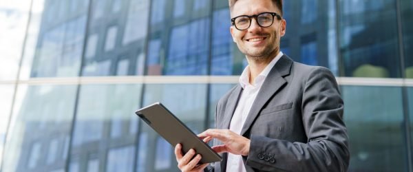 A,Cheerful,Businessman,In,A,Suit,Holds,A,Tablet,,Standing